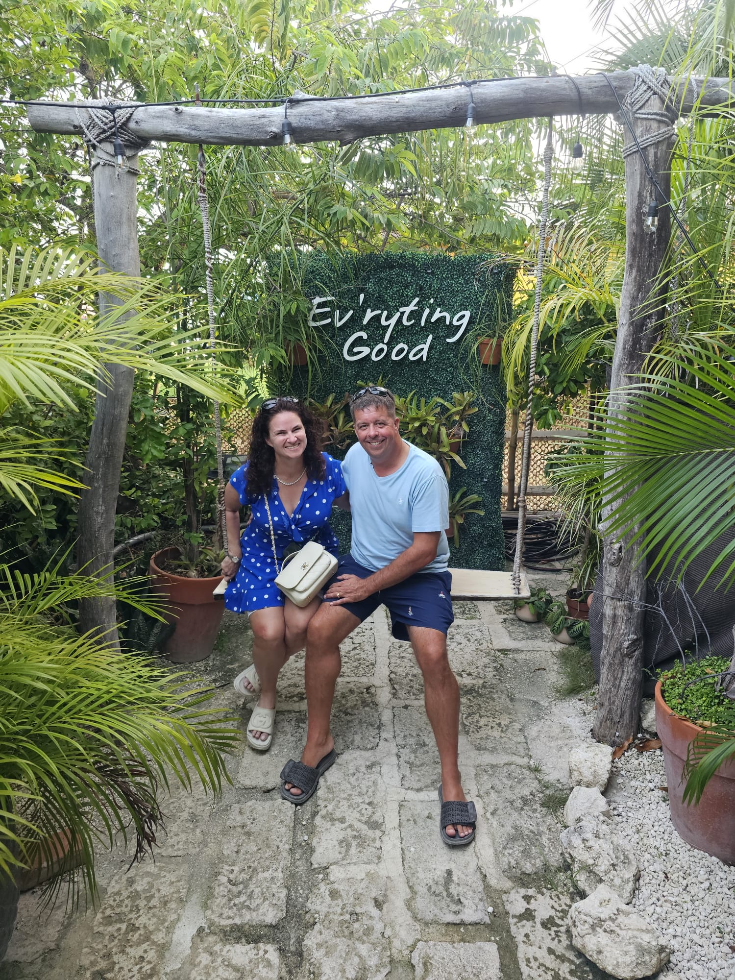 Couple beneath an Everything Good sign at a Barbados garden stop
